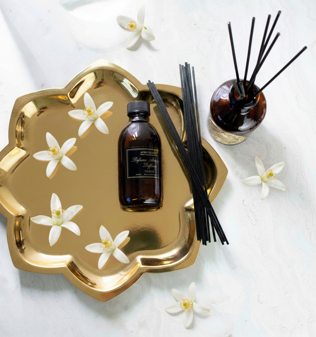 Africology Neroli Diffuser and 200ml Neroli refill on a gold tray with neroli blossoms on white marble