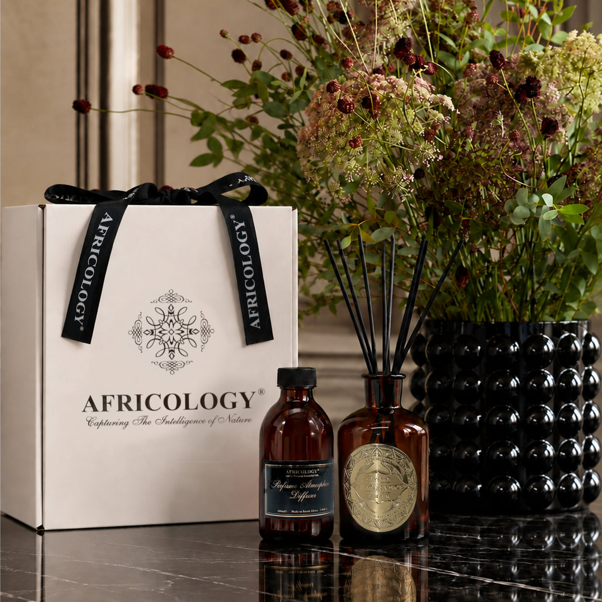 Africology reed diffuser, refill and white gift box styled with dried florals on dark marble